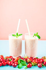 two glasses of smoothies made from milk, strawberries, banana, cherries, decorated with mint on bright pink blue background Concept healthy lifestyle, diet, tasty Copy space