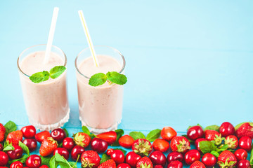 two glasses of smoothies made from milk, strawberries, banana, cherries, decorated with mint on bright blue background Concept healthy lifestyle, diet, tasty Copy space