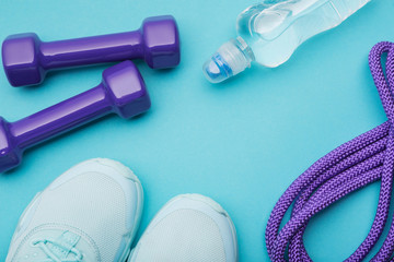 Fototapeta na wymiar turquoise sneakers, a bottle of water, lilac dumbbells and a skipping rope on a turquoise background, minimalism, concept fitness and water