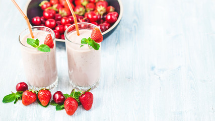 two glasses of smoothies made from milk, strawberries, banana, cherries, decorated with mint on bright white background Concept healthy lifestyle, diet, tasty Copy space