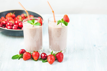 two glasses of smoothies made from milk, strawberries, banana, cherries, decorated with mint on bright white background Concept healthy lifestyle, diet, tasty Copy space
