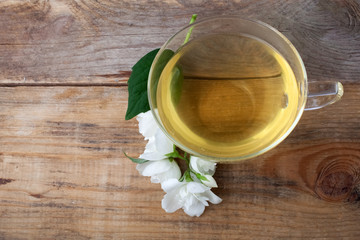Glass cup of tea with jasmine flowers on wooden background.. Top view