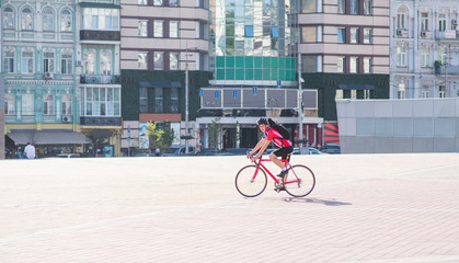 Portrait of a man cyclist who rides a red bike in the city. A cyclist in red sportswear and a helmet rides a city bike in the background of architecture