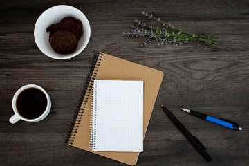 Open blank notepad, pen, lavender, coffee and cookies on the dark wooden table. Workplace flat lay