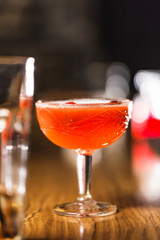 Three colorful cocktails in large glasses in a classic bar environment with dozens of blurry liquor bottles in the background.
