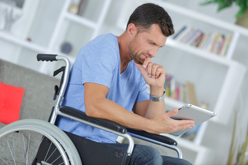 disabled man in wheelchair using digital tablet at home