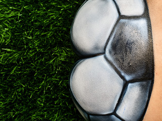 the ass of a naked girl with a beautiful waist, painted in a soccer ball, sits on the green grass. Beautiful body art on the theme of football on a black background - 208147653