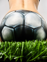 the ass of a naked girl with a beautiful waist, painted in a soccer ball, sits on the green grass. Beautiful body art on the theme of football on a black background - 208147694