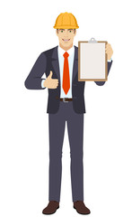 Businessman in construction helmet showing thumb up and holding clipboard