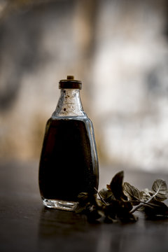 Ayurevedic essence or oil of holy basil or tulsi in a transparent bottle with some fresh bright basil leaves on wooden surface used in many treatments and home remedies related to cough, and fever.