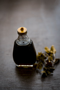 Ayurevedic essence or oil of holy basil or tulsi in a transparent bottle with some fresh bright basil leaves on wooden surface used in many treatments and home remedies related to cough, and fever.