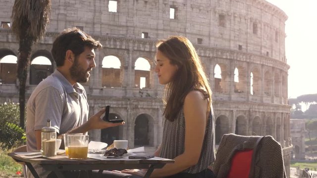 Happy couple marriage proposal with ring sitting at restaurant in front of colosseum in rome at sunset emotional