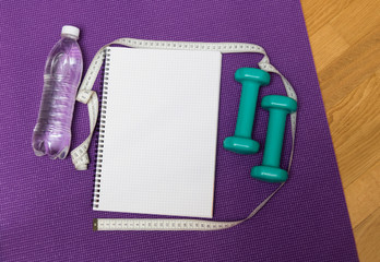 Bottle of  water, notebook and  dumbbells on yoga mat