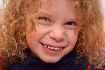 Kleiner Junge mit lockigen Haaren zieht eine lustige Grimasse und zeigt seine Zähne