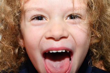 Kleiner Junge mit lockigen Haaren lacht herzlich mit offenem Mund in die Kamera