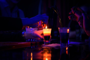 bartender makes burning alcoholic cocktail in shot glass on a table at night club