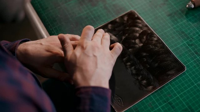 The master applies a softening cream to the skin. The process of manufacturing a travel case made of genuine leather. Handmade. Macro shooting.