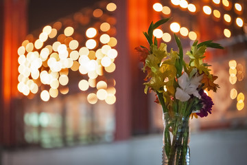 Bouquet with flowers in the vase made hastily of a plastic bottle against the background of fires of ritual candles.