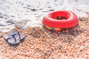 Summer shells beach with children's flip flops mask and donut for swimming in the sea.