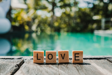 .Small wooden letters forming the word love on the edge of a pool with crystal blue water. Love concept. Lifestyle