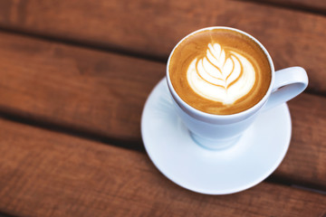 A cup of coffe with latte art on wooden table. Shot at angle with selective focus, italian cappuccino.