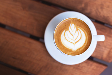 A cup of coffe with latte art on wooden table. Top view, morning mood, italian cappuccino. With place for text.