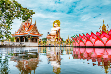 Wat Plai Laem Buddhism Temple statues during a bright sunny day with lake in the foreground in Koh...