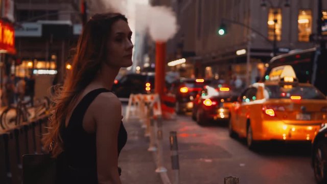 Young beautiful woman standing near the traffic road close to smoke pipe in New York, America and waits for taxi.