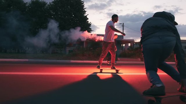 Group of young people skateboarding on the road in the early morningwith red sugnal flare, slow motion