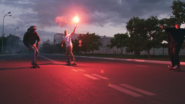 Group of young people skateboarding on the road in the early morningwith red sugnal flare, slow motion