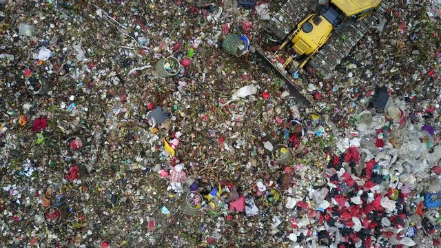 Overhead drone shot of excavator dumping trash onto garbage dump, while people scavenge through the rubbish at the Bantar Gebang landfill in Jakarta, Indonesia