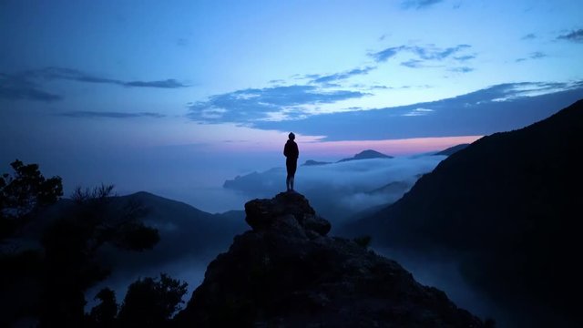 Woman on cliff above coastline of Corsica with remote beach and covered in fog after sunset