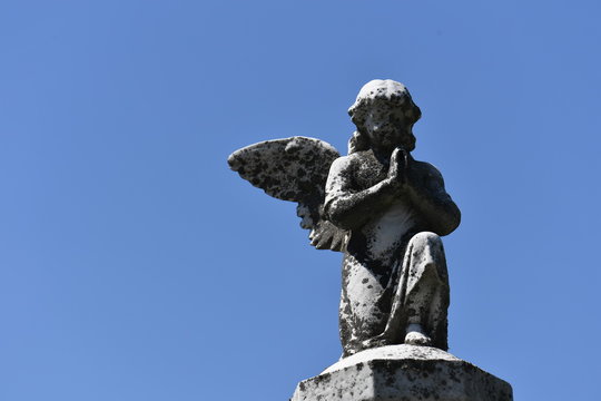 A weathered sculpture of a praying angel on a tomb of the cemetery of Quebec-Canada. A warm and sunny spring day
