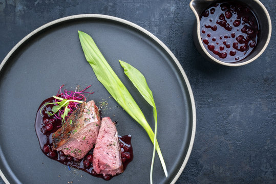 Traditional barbecue dry aged sliced venison fillet steak with wild garlic and cowberry sauce as top view on a plate with copy space