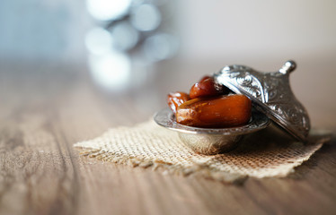 Fresh fruit dates in a silver metal bowl on a piece of sackcloth on walnut wooden table - obrazy, fototapety, plakaty