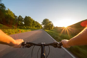 Foto op Plexiglas Fietsen Hands holding handlebar of a bicycle with green meadow on background. View from bikers eyes.