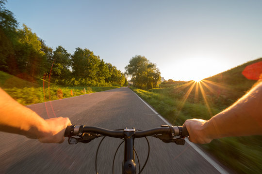 Hands holding handlebar of a bicycle with green meadow on background. View from bikers eyes.