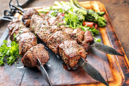 Traditional Russian shashlik on a barbecue skewer with green asparagus and paprika as close up on a burnt cutting board