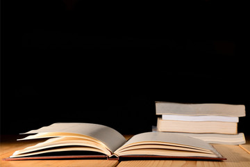 Opened book and pile of book on wooden table against black background.