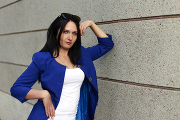 Beautiful girl with a mysterious smile in a blue jacket posing near the wall and looking straight