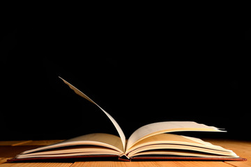 Book was open on wooden table and black background.