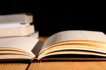 Opened book and pile of book on wooden table against black background.