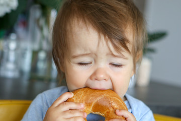 Portrait of funny little baby boy eating big bagel with closed eyes, fun face expression, close-up, teething child
