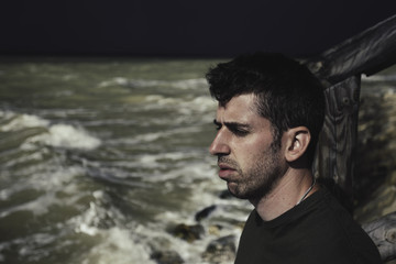 Young man looking at the mediterranean sea, with stormy sky background at the beach