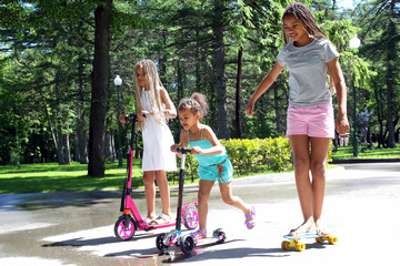 Three girls go together on a skateboard and roller skates