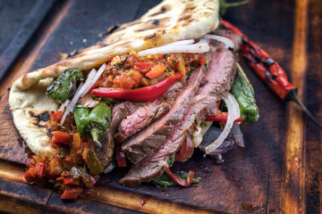 Barbecue dry aged wagyu flank steak chili relish and vegetable in a flatbread on a burnt board