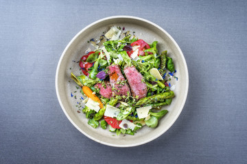 Modern spring salad with barbecue dry aged sliced fillet steak and green asparagus as top view on a...