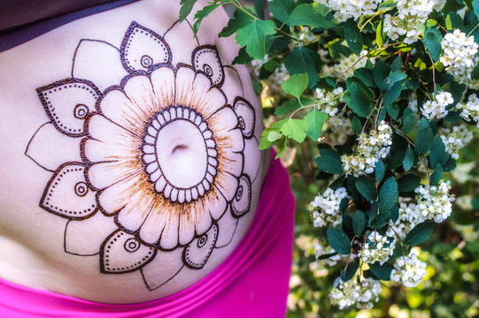 close-up of the belly of a pregnant woman with a henna pattern on a background of flowers. concept beauty of pregnancy