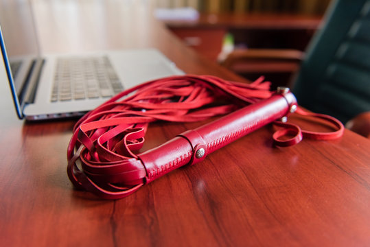 Red leather whip on table with laptop