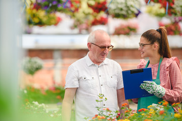 Man and woman in greenhouse looking flowers. Woman salesman serving customer in garden center.